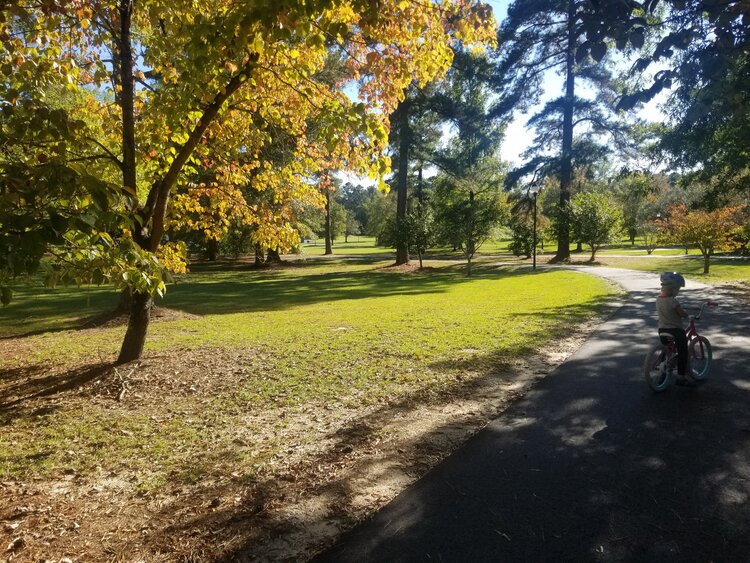 A small child adjusting her bike on a paved trail at Scott Park