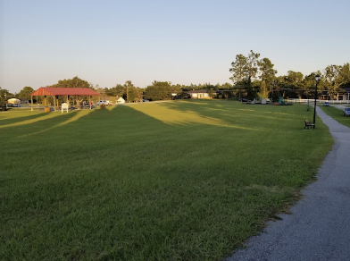 Green field inside a walking trail, with a picnic shelter in the distance