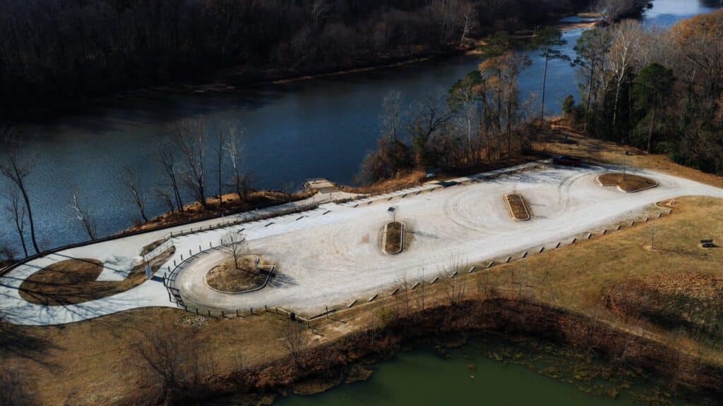 Aerial view of an empty, curved gravel parking lot by a river, surrounded by trees in winter.