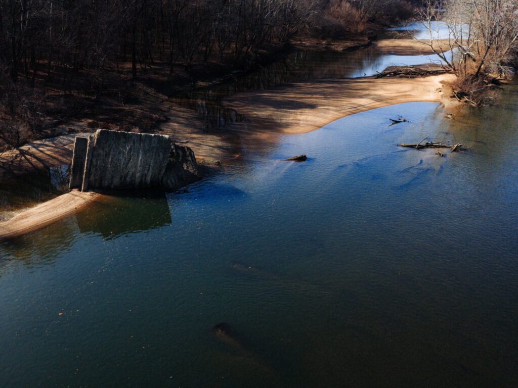 A concrete structure juts into a calm river, surrounded by sandbanks and leafless trees.